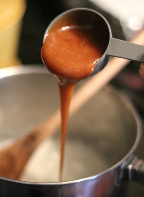 Caramel sauce being added to melted marshmallow mixture in a saucepan