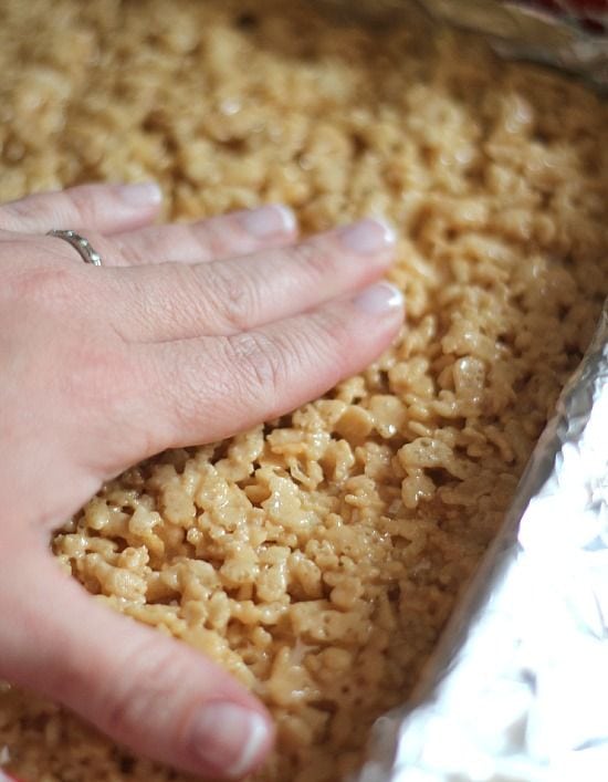 Caramel rice krispie treat layer being pressed over peanut butter blondie and marshmallow layers in a pan