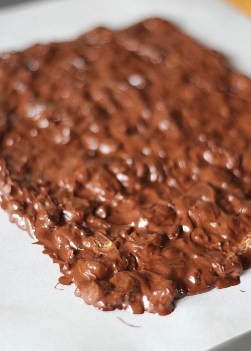 Melted chocolate peanut butter mixture spread on a parchment-lined sheet pan