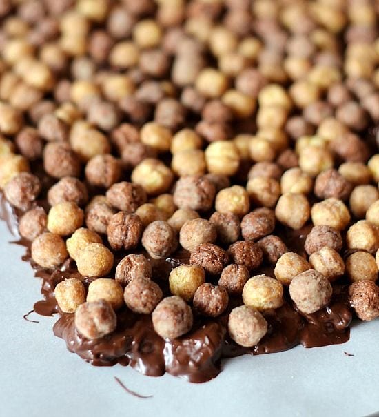 Reeses puffs cereal over melted chocolate peanut butter mixture in a sheet pan