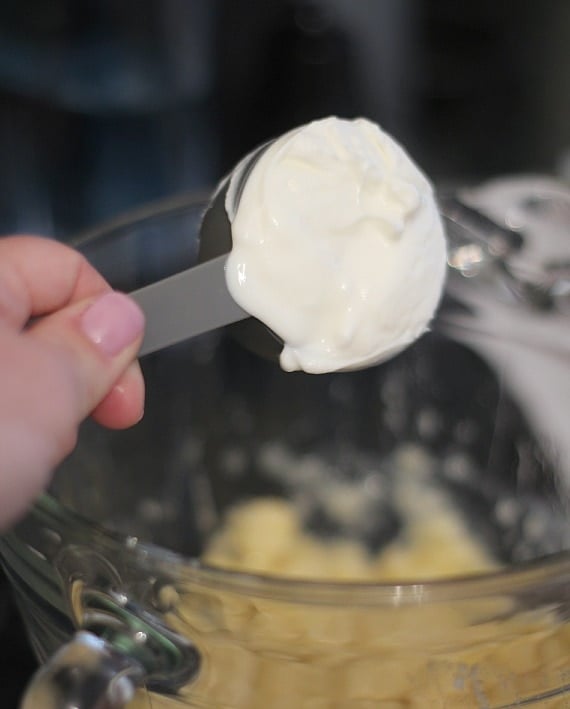 A measuring cup of sour cream being poured into a mixing bowl