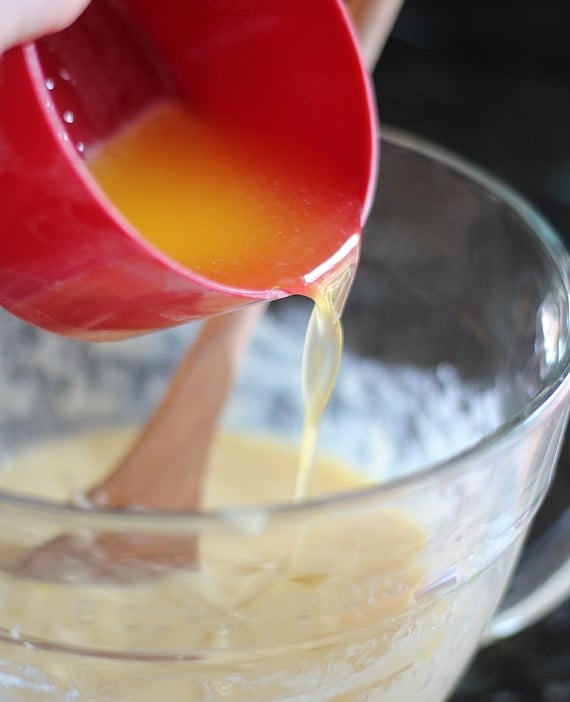 A cupful of melted butter being poured into a mixing bowl