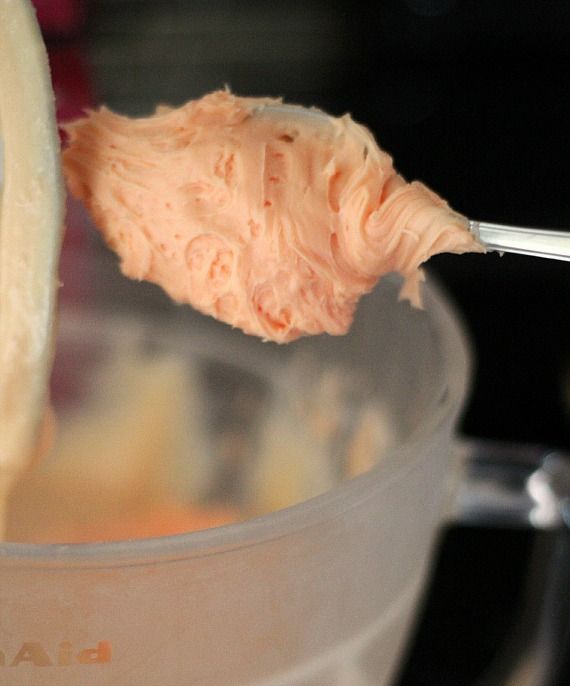A spoonful of orange frosting over a mixing bowl