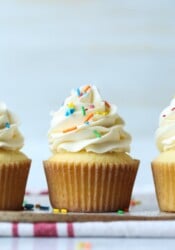 Three fluffy, soft vanilla cupcakes topped with swirls of vanilla frosting and sprinkles in a row.