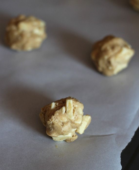 Cookie dough balls with white chocolate chunks on a parchment-lined baking sheet