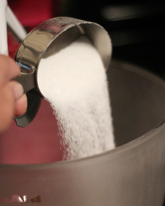A measuring cup of granulated sugar being added to a mixing bowl