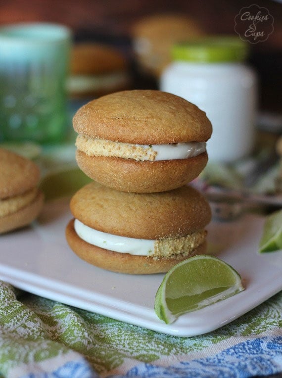 Two key lime whoopie pies stacked on a white plate next to a lime wedge.