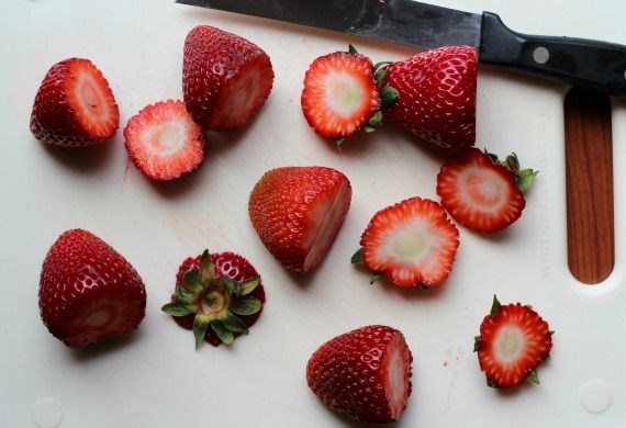 Fresh strawberries on a cutting board with the tops sliced off
