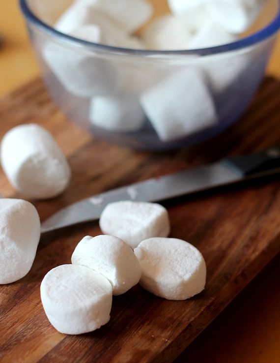 A bowl of marshmallows and halved marshmallows on a cutting board
