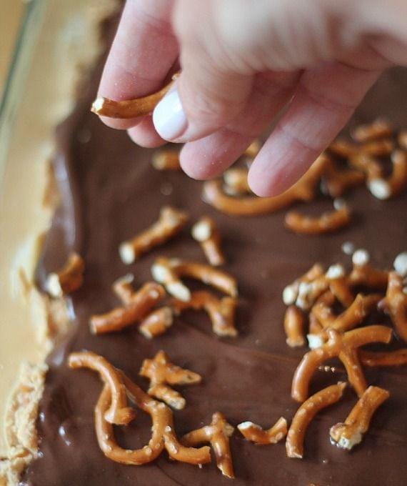 Mini pretzel pieces being spread over chocolate peanut butter bars in a pan