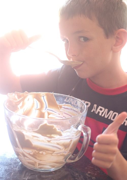 A little boy licking a bowl of batter and giving the thumbs up sign