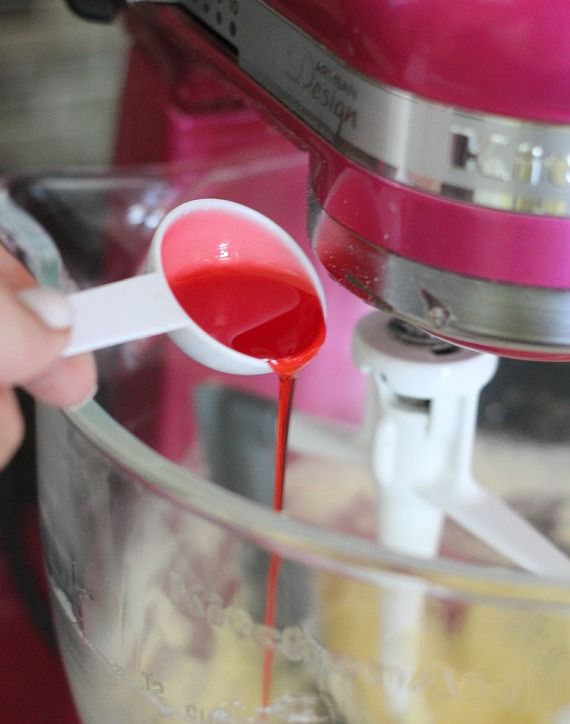 Red strawberry syrup being added to a stand mixer bowl