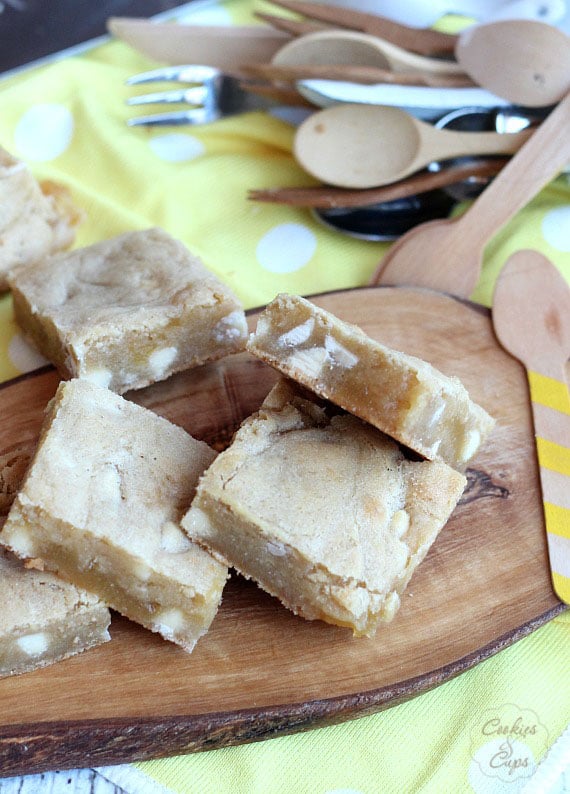 Assorted white chocolate lemon blondie on a wooden platter with utensils in the background.