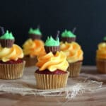 A mini halloween cupcake frosted with orange frosting and topped with a mini peanut butter cup and green icing meant to look like a cauldron