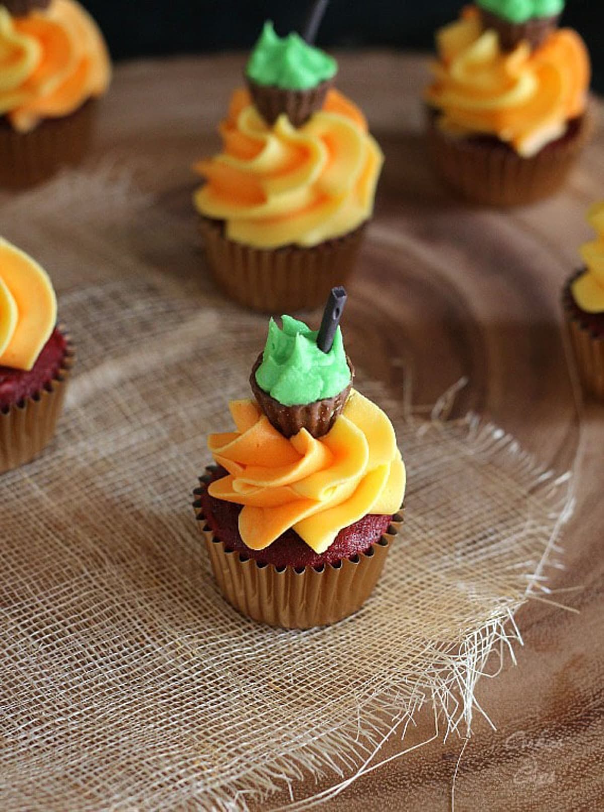 A mini red velvet cupcake topped with a swirl of orange frosting and topped with a peanut butter cup made to look like a cauldron.