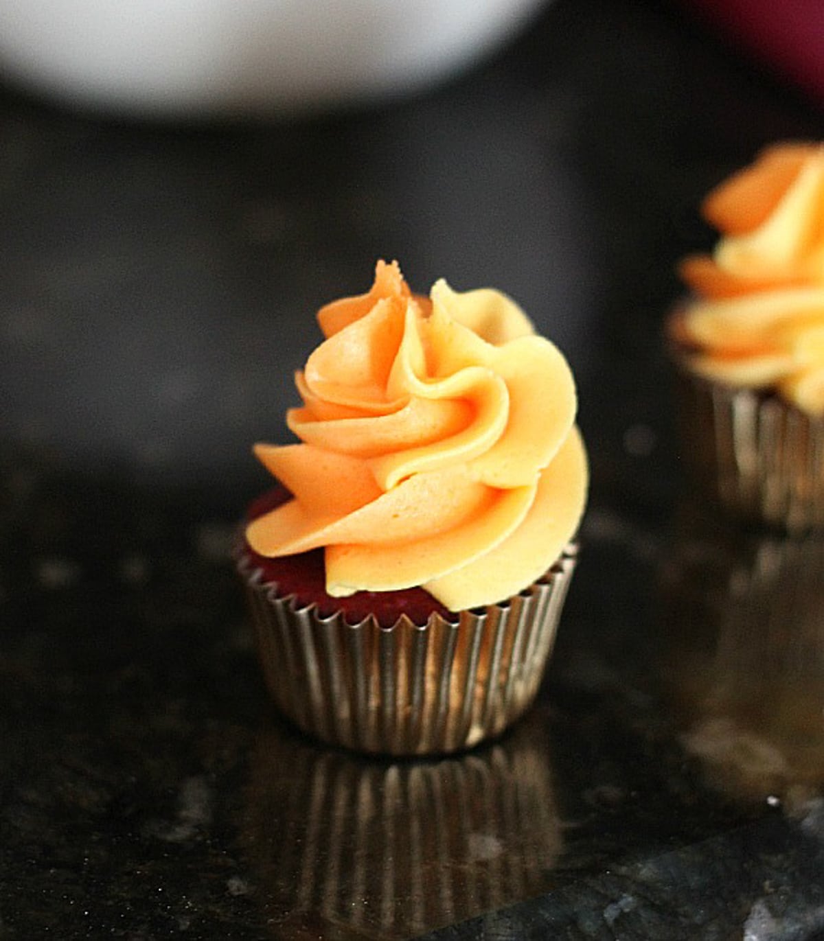 A mini cupcake topped with a swirl of orange frosting.