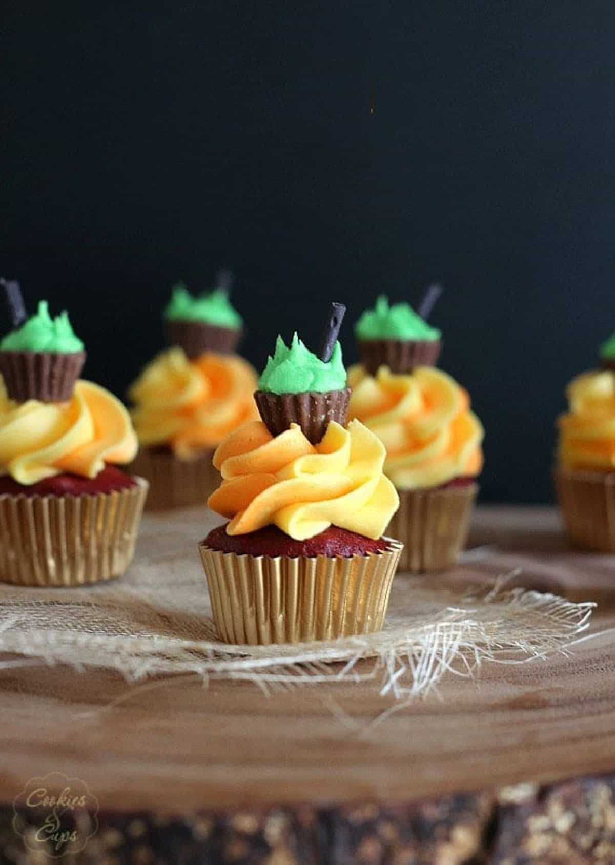 A mini halloween cupcake frosted with orange frosting and topped with a mini peanut butter cup and green icing meant to look like a cauldron