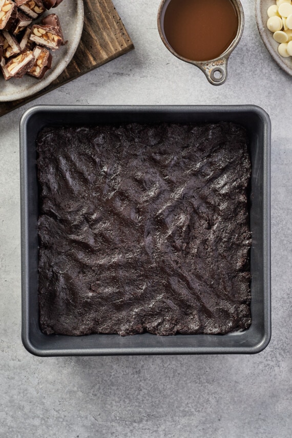 The first layer of chocolate batter is spread in the bottom of a baking pan.