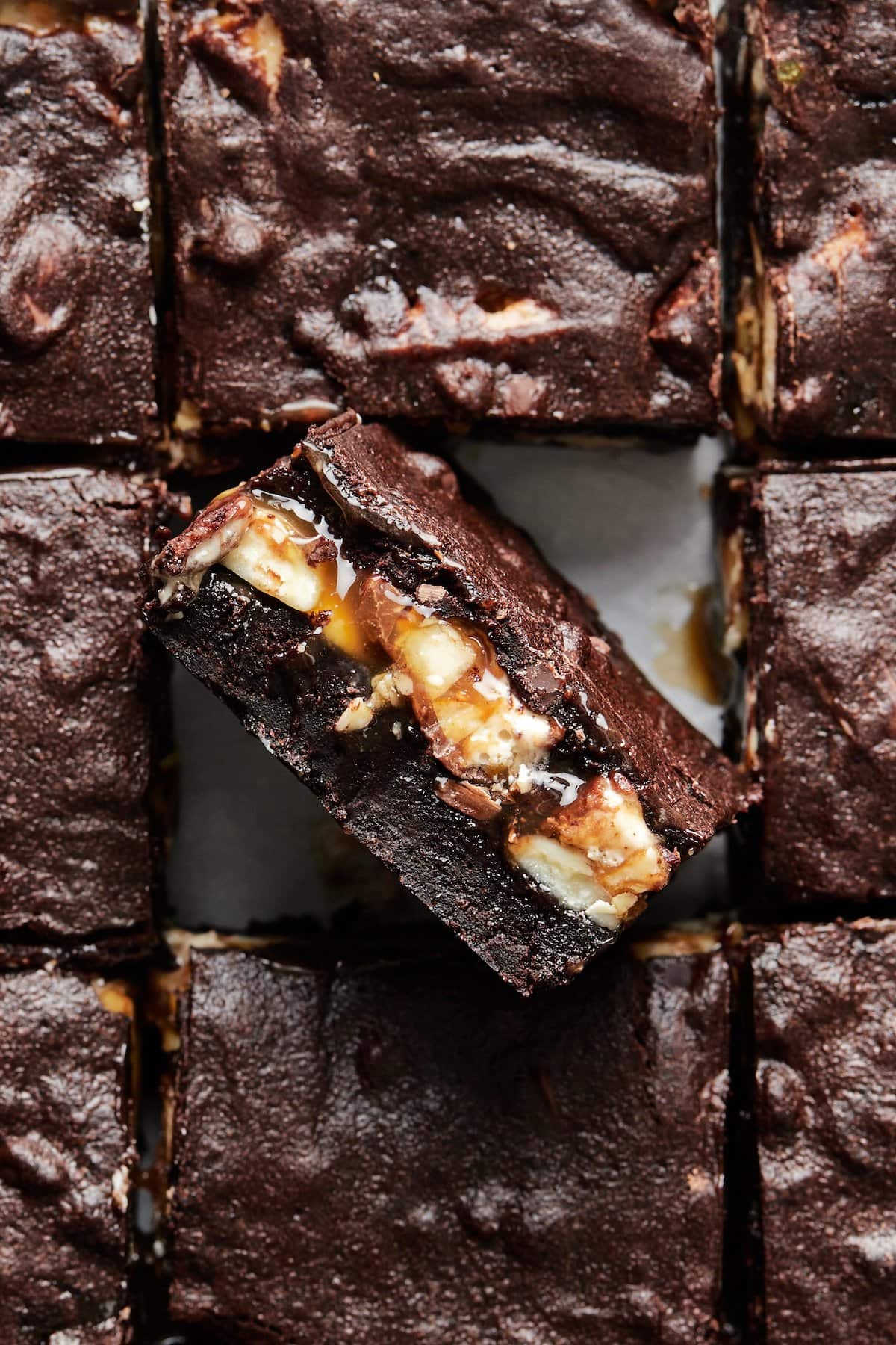 Close up of layered brownie bars, with one turned on its side to reveal the Snickers layers.