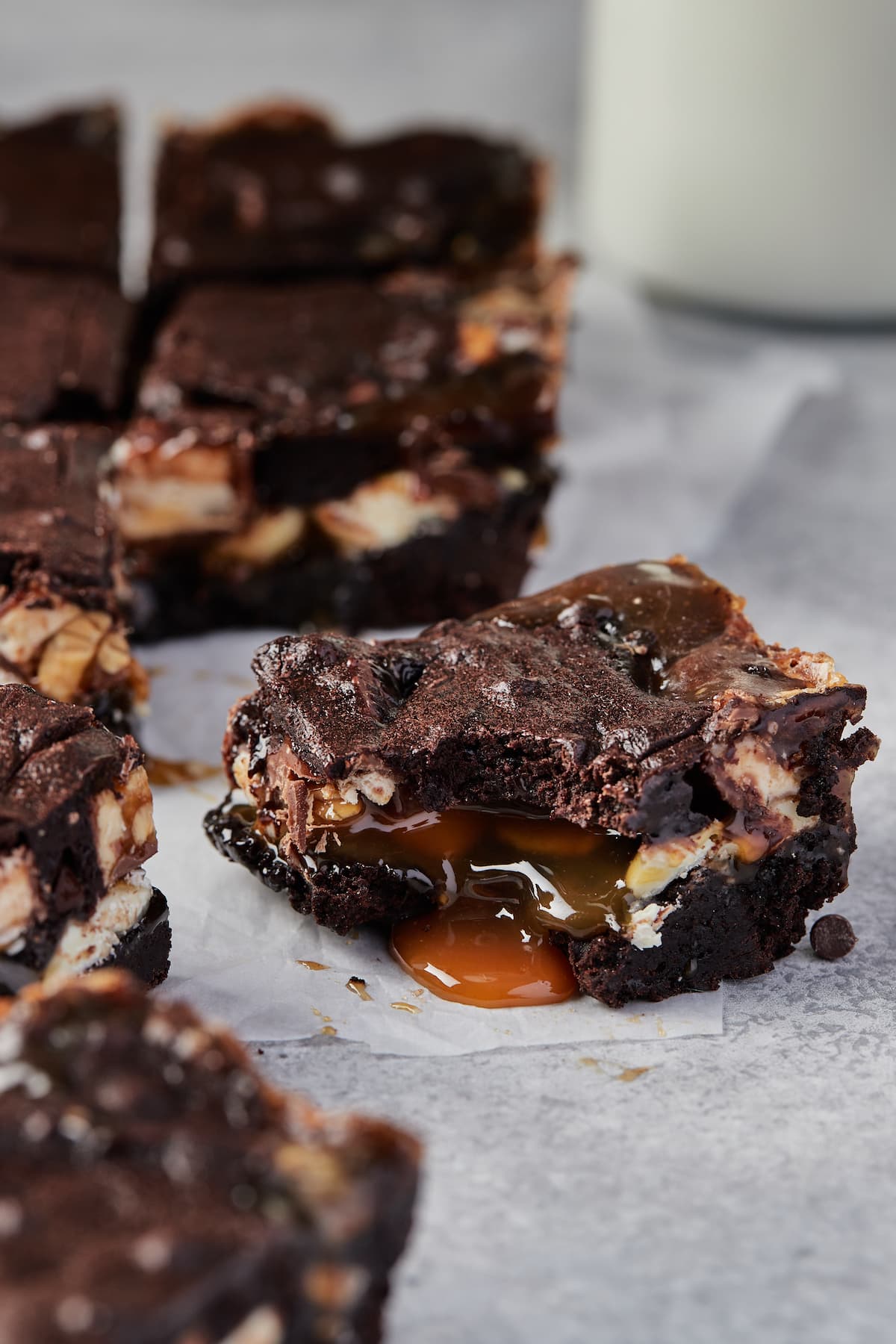 Caramel oozes out from a Snickers brownie, with more brownies scattered in the background.