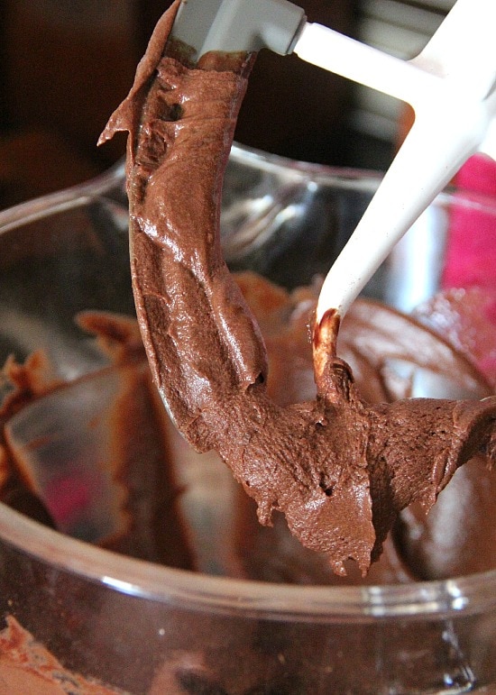 These soft chocolate brownies are kid-approved, frosted with a thin layer of fudgy icing that you pour on top while the brownies are warm. A mixer attachment dripping with brownie batter over a bowl.