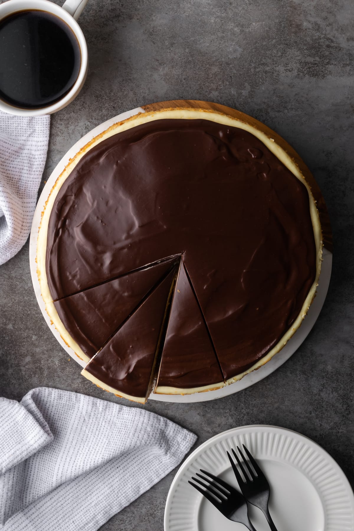 Top view of a Boston Cream Pie cheesecake with two slices cut from it, next to plates and forks.