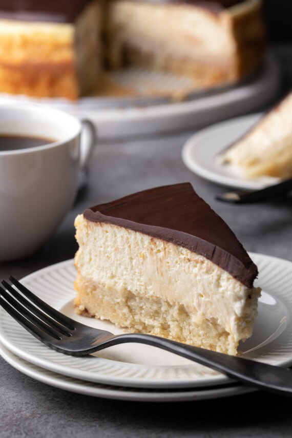 A slice of Boston Cream Pie cheesecake on a plate next to a fork.
