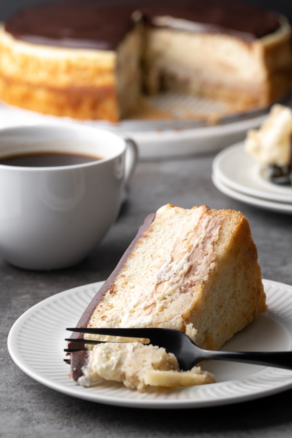 A slice of Boston Cream Pie cheesecake on a plate, laying on its side next to a fork.