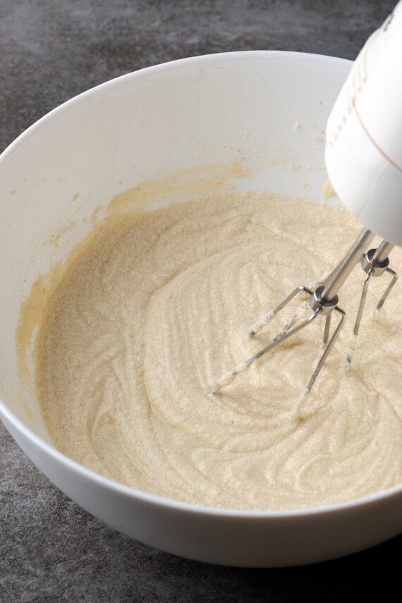 A mixer is used to combine cake batter in a mixing bowl.
