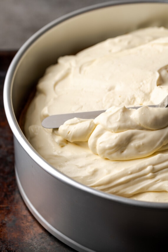 Cheesecake mixture is spread over the cake layer in a springform pan.