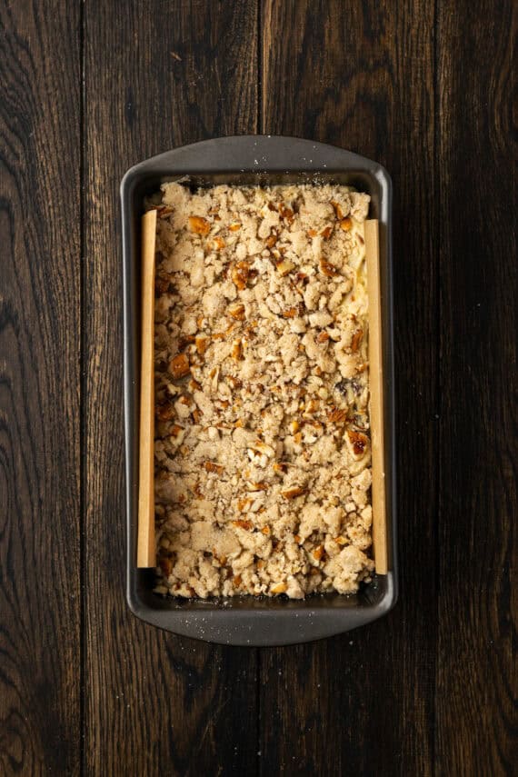 Apple pie bread batter in a lined loaf pan, topped with streusel.