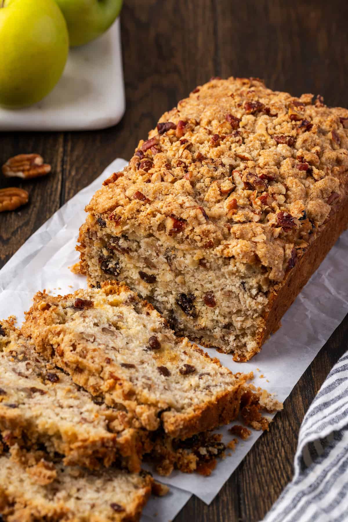 A loaf of apple pie bread with slices cut from the end, with Granny Smith apples in the background.