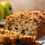 Front view of a loaf of apple pie bread with slices cut from the end, with Granny Smith apples in the background.