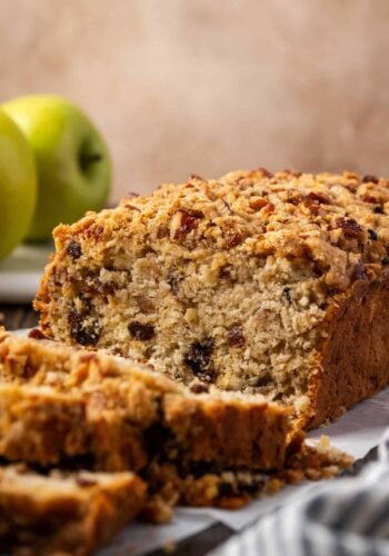 Front view of a loaf of apple pie bread with slices cut from the end, with Granny Smith apples in the background.