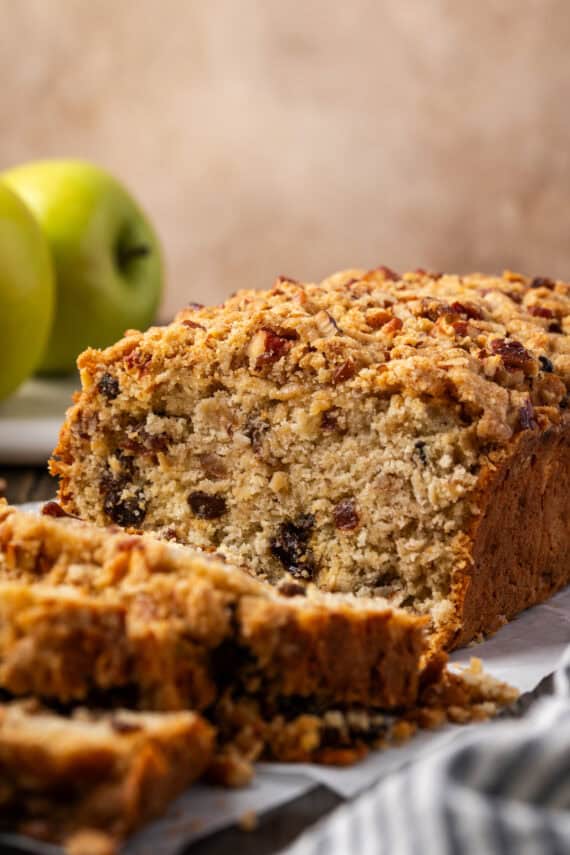 Front view of a loaf of apple pie bread with slices cut from the end, with Granny Smith apples in the background.