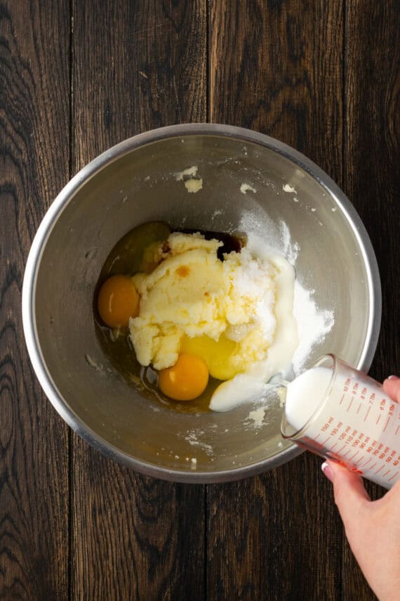 Buttermilk is poured into apple pie bread ingredients in a metal bowl.