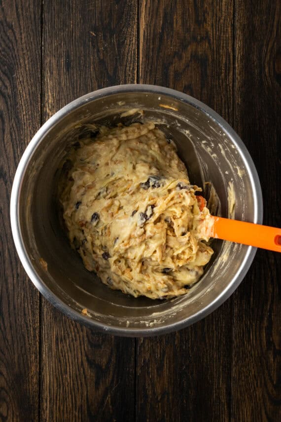 Apple pie bread batter in a metal mixing bowl with an orange rubber spatula.