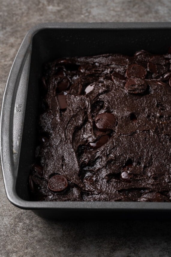Cake mix brownie batter spread into a square metal baking pan.