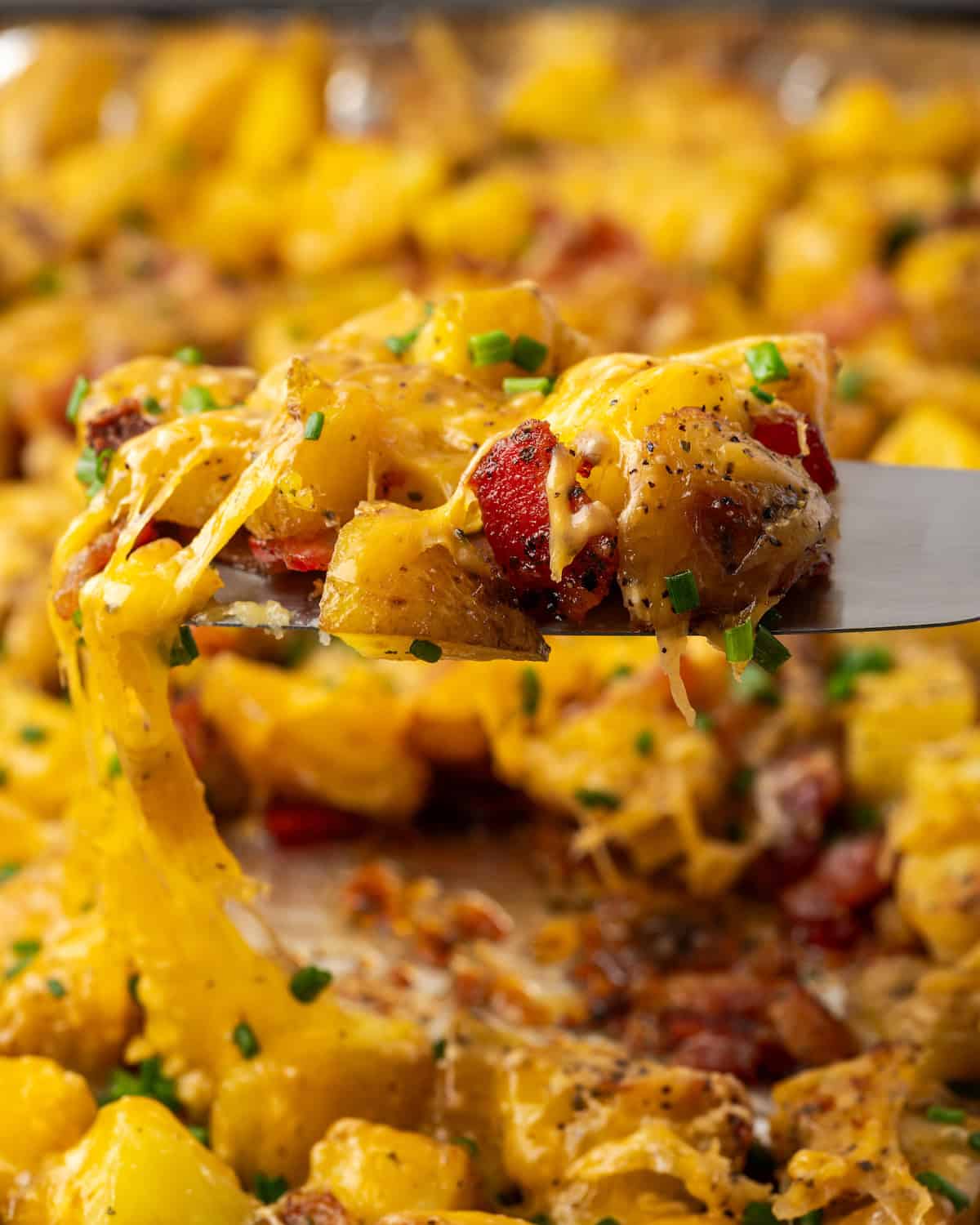 Close a spatula scooping Cheesy Ranch potatoes from a baking sheet.