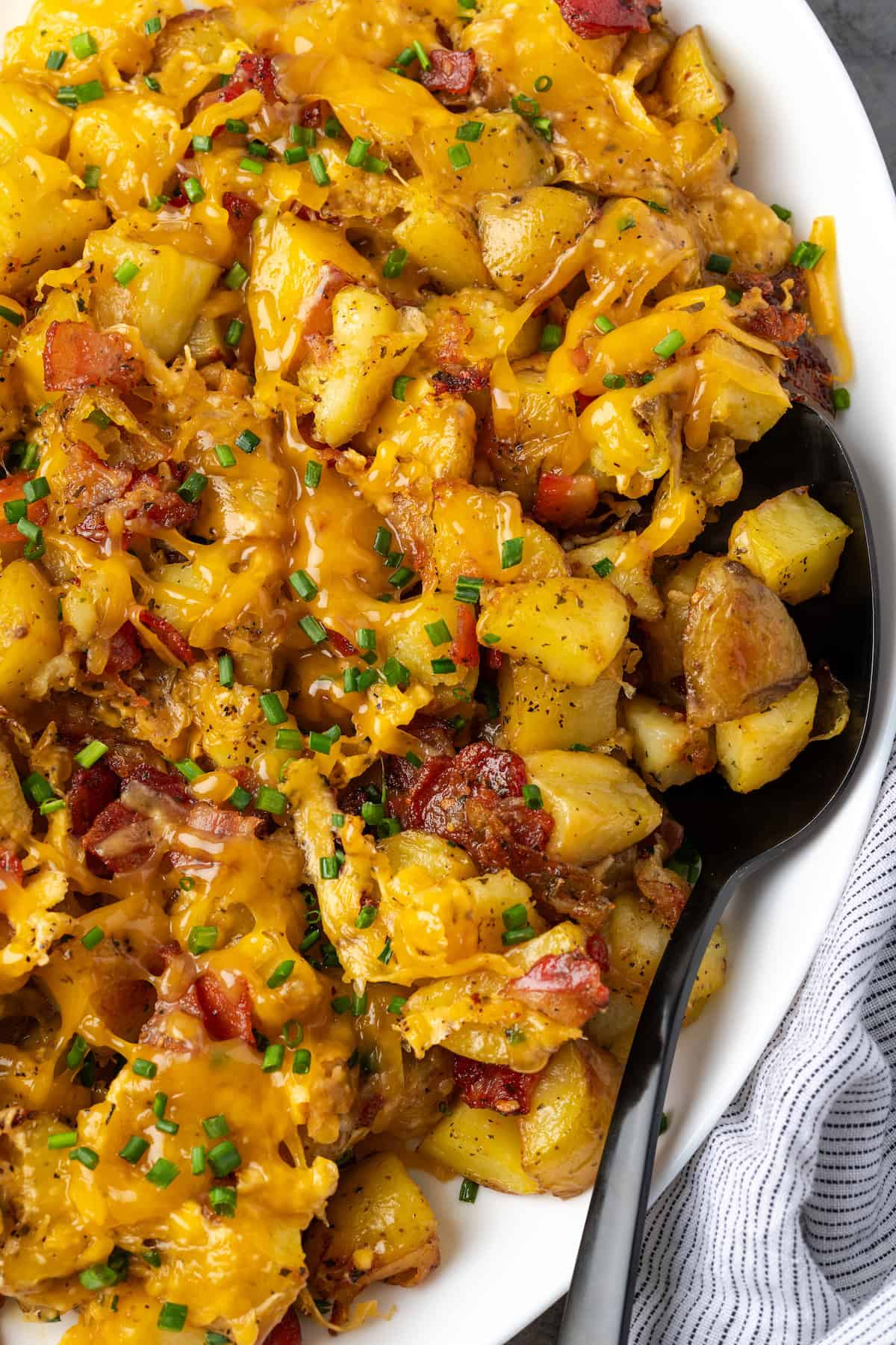 Overhead view of cheesy ranch potatoes on a white platter with a spoon for serving.