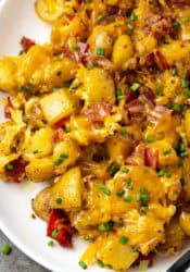 Close up of cheesy ranch potatoes on a white platter.