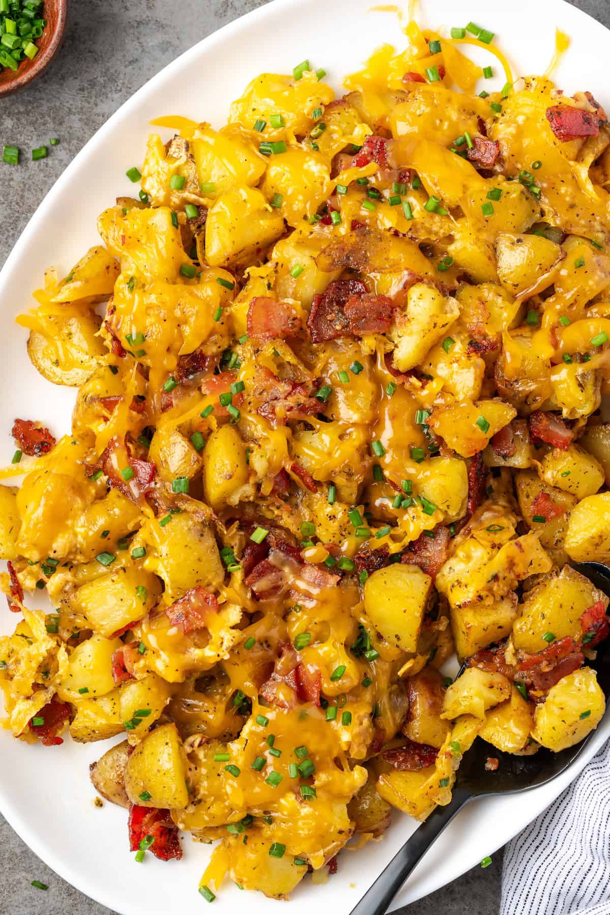 Overhead view of cheesy ranch potatoes on a white platter with a spoon for serving.