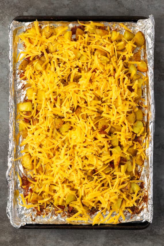 Roasted ranch potatoes with shredded cheese on a lined baking sheet.