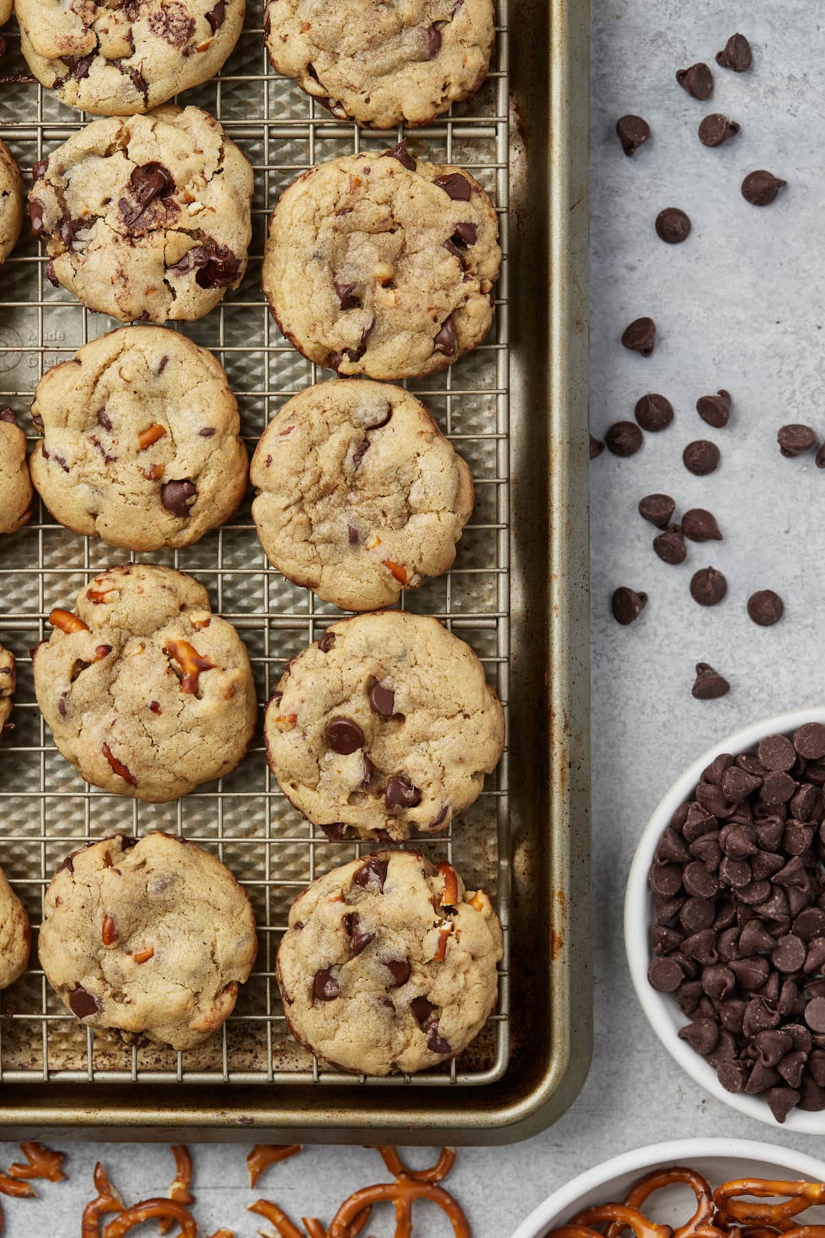 Close up of a corner of a baking sheet with rows of salty pretzel chocolate chip cookies, next to a bowl of chocolate chips.