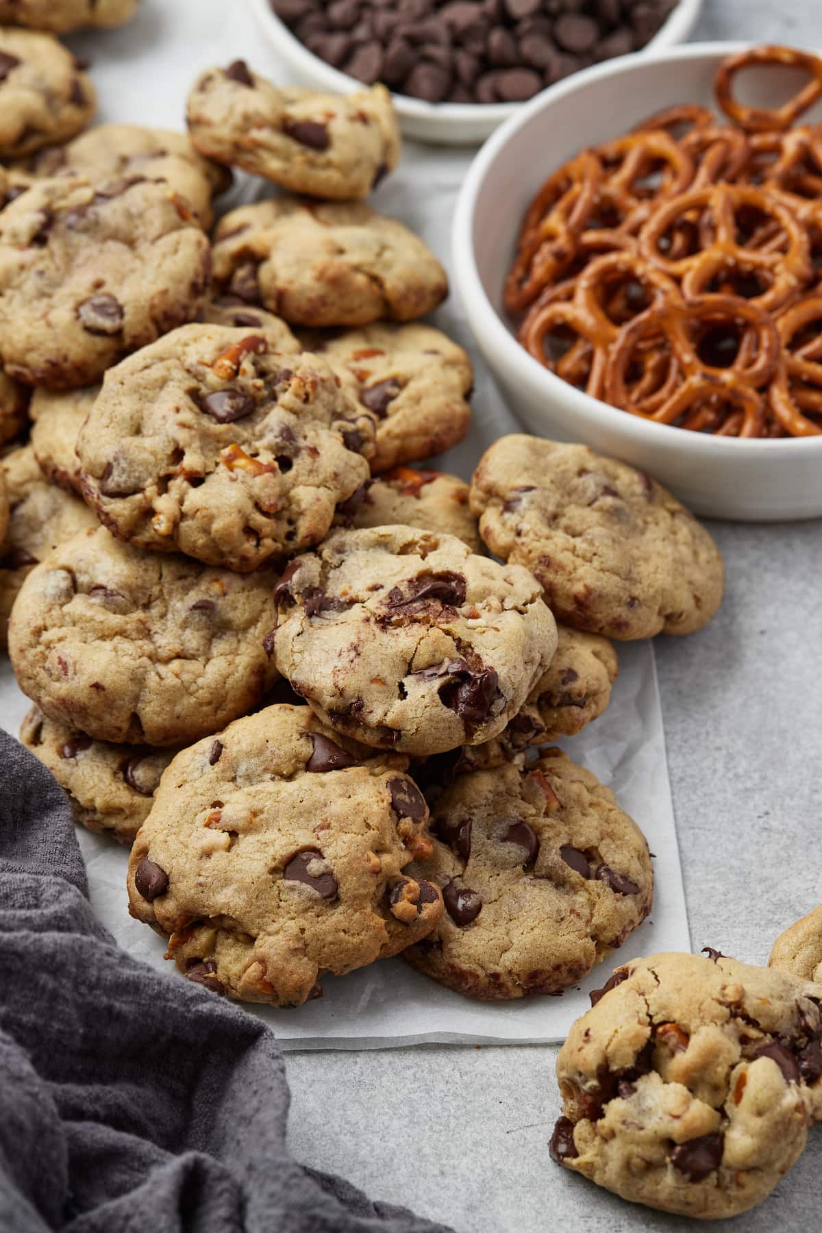 An assortment of salty pretzel chocolate chip cookies next to bowls of mini pretzels and chocolate chips.