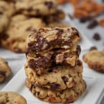 Salty pretzel chocolate chip cookies stacked on a square white plate, surrounded by cookies.