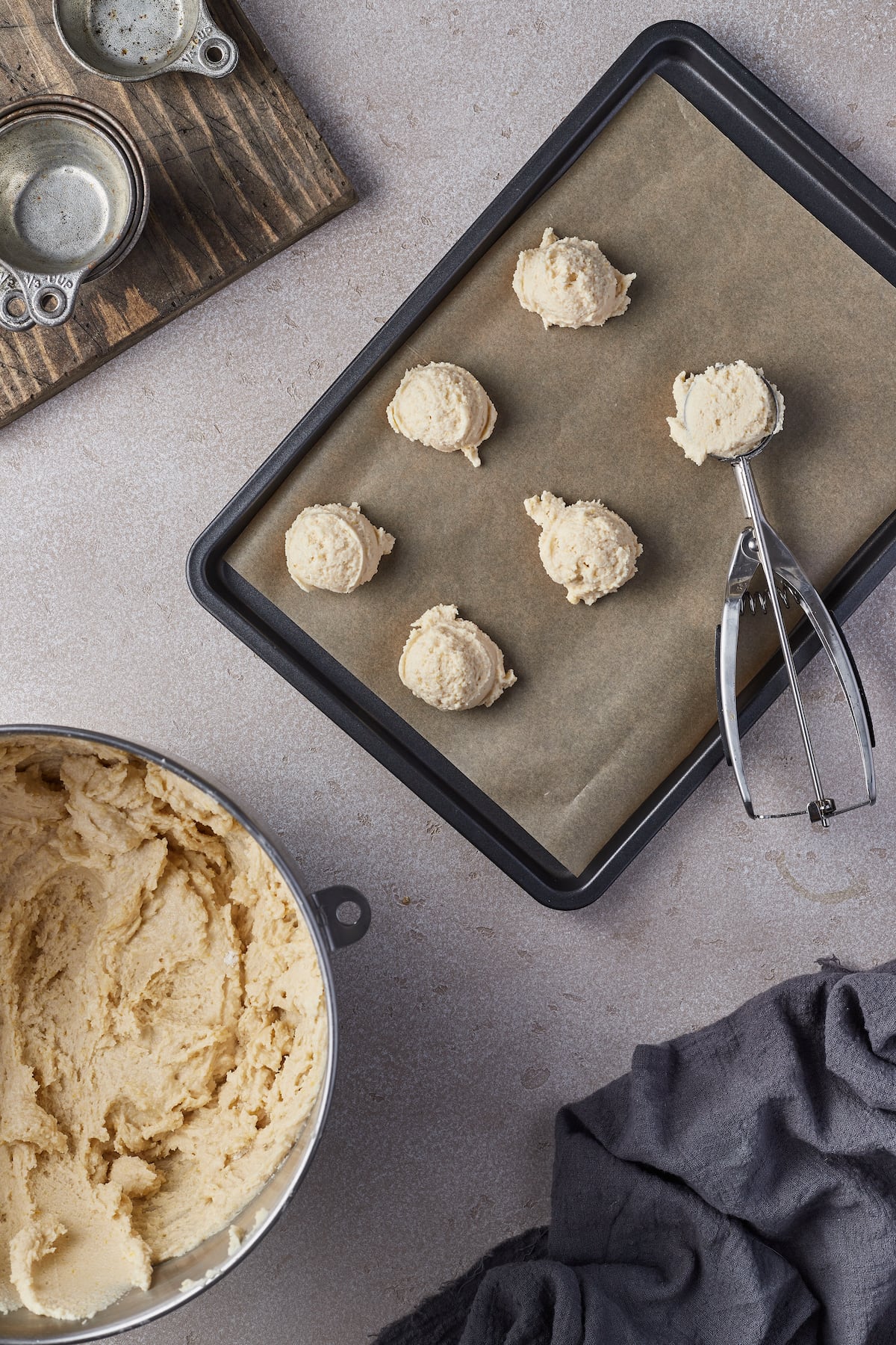 Sugar cookie balls on a baking sheet next to a cookie scoop.