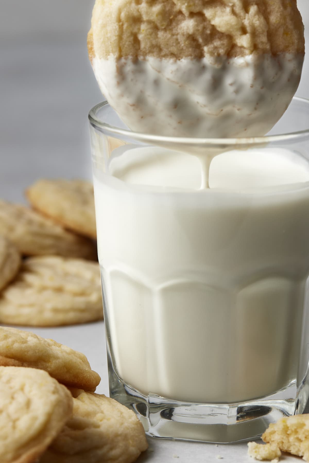 A sugar cookie is dunked into a glass of milk.