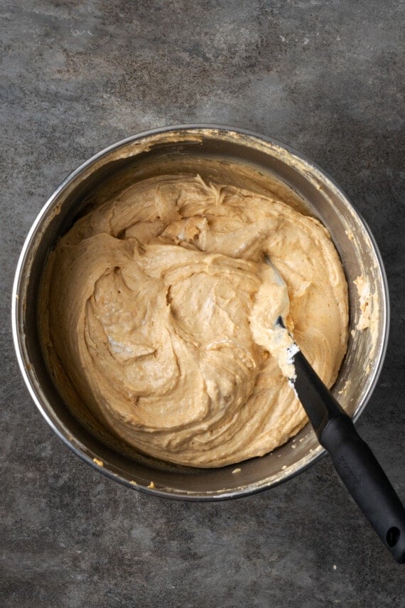 Peanut butter cheesecake filling stirred together in a metal mixing bowl with a black spoon.
