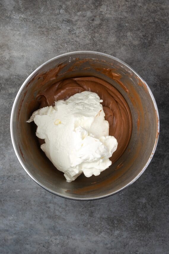 Whipped cream added to the chocolate cream cheese mixture in a mixing bowl.